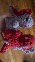 Two small crocheted toys, one gray and one red, on a wooden surface.